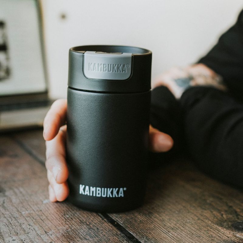 Kambukka Olympus insulated tumbler - coffee cup - 300ml - black - person holding it in hand on a table.