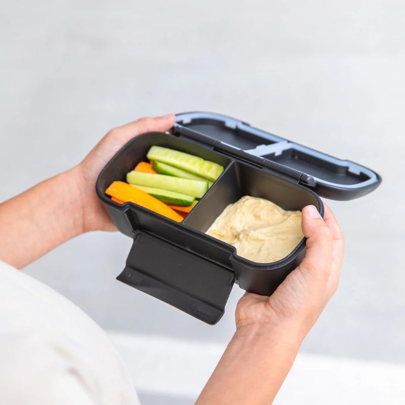  MontiiCo snack lunch box - hands holding snack box with food in. 