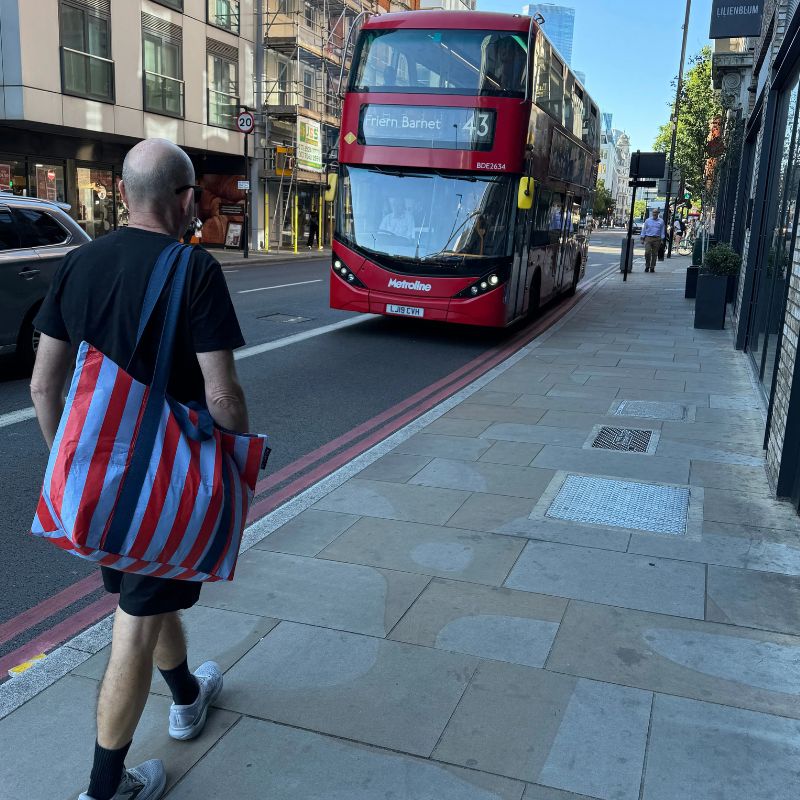 Project Ten Zip Medium Tote - hanging on mans shoulder next to a bus. 