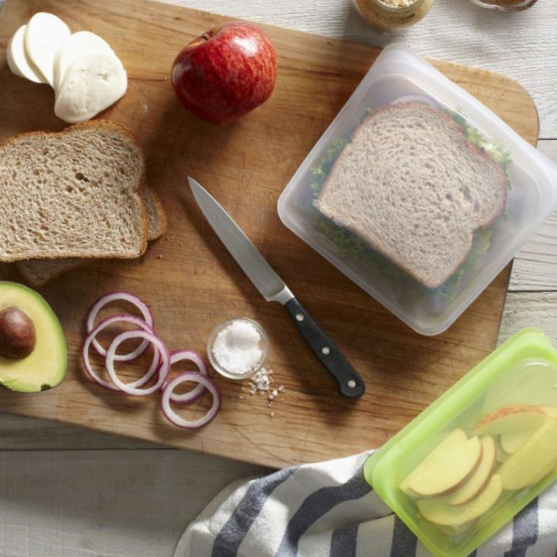 Stasher reusable silicone sandwich bag 828ml - on table top with food and sandwich inside.