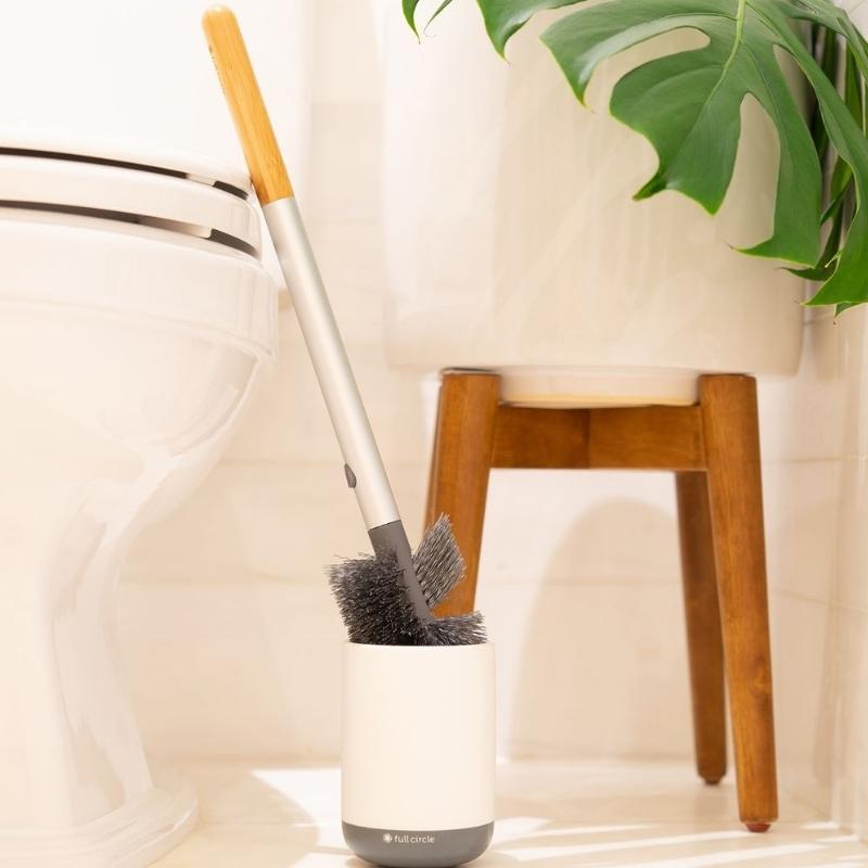 Full Circle Scrub Queen Toilet Brush - comes with replaceable brush head - shown next to a toilet and a plant. 