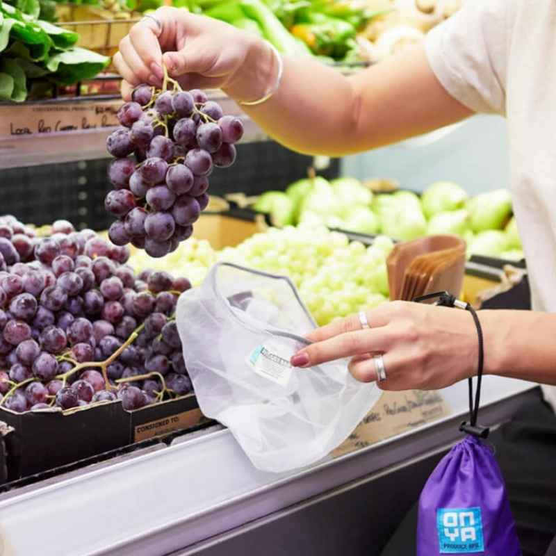 Onya reusable mesh produce bags includes a pouch to keep the bags in. Photo from supermarket filling grapes in a bag.